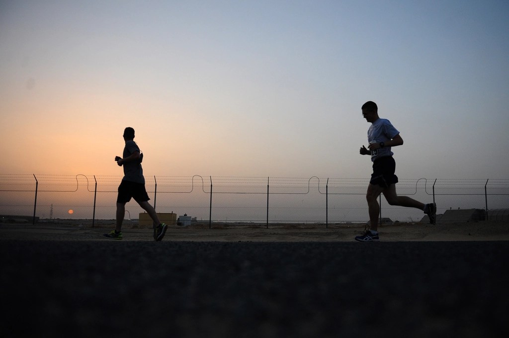 Two people running along the fence, with the sun setting down in the background.