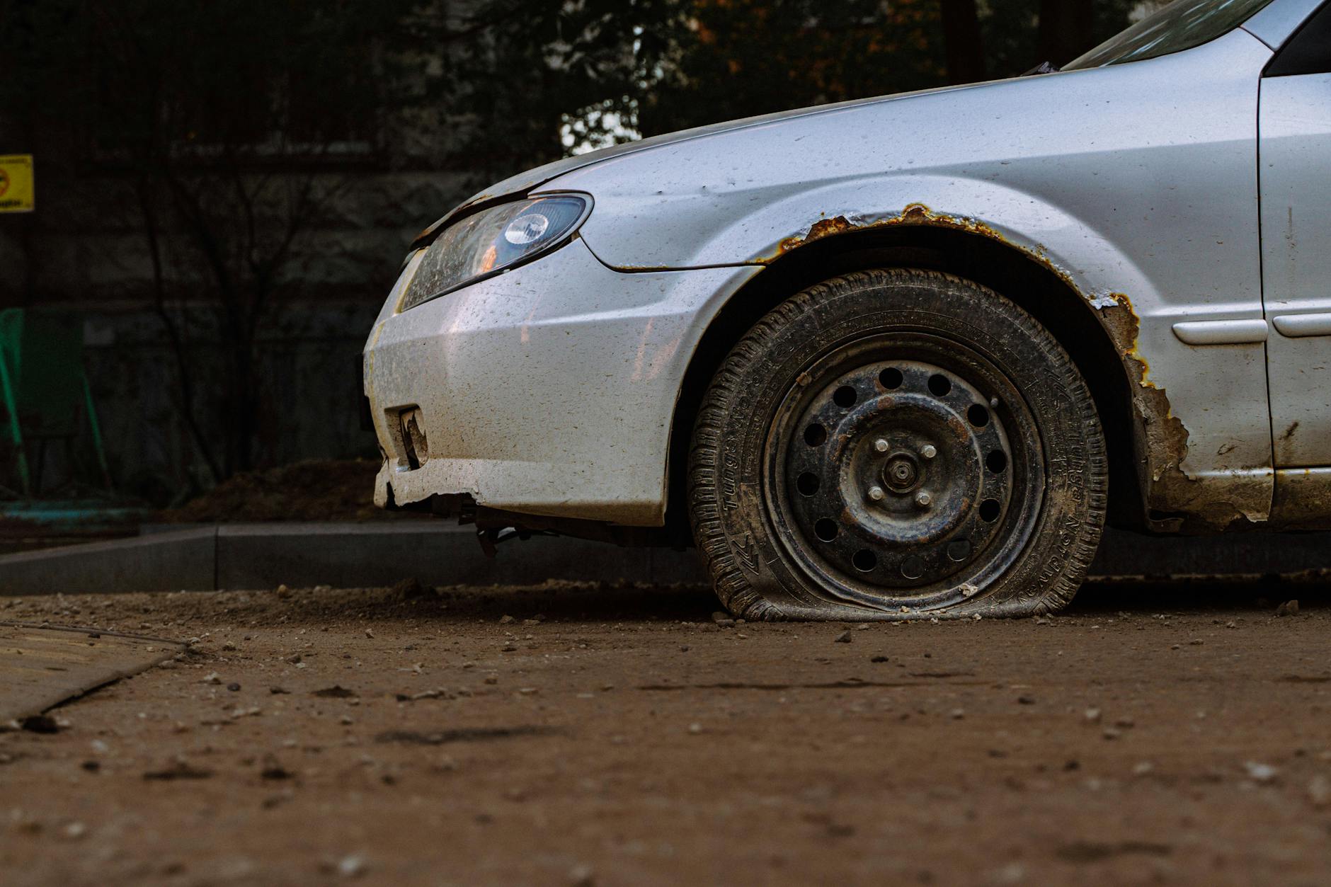 The front driver-side of a car parked with a flat tire on the front wheel.