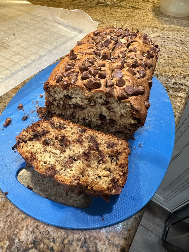 Banana bread lying on top of a blue cutting board, after a slice was cut from it.