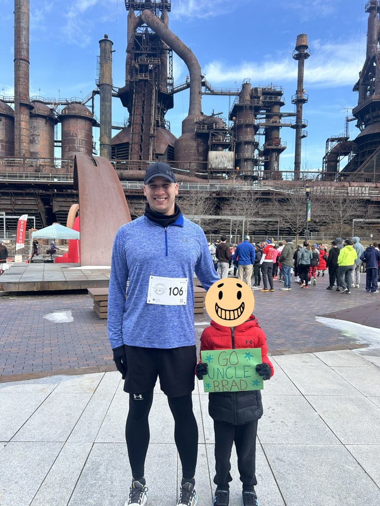 Me and my nephew at my race. I had my racing bib on with the race number 106. My nephew next to me is holding a green sign that says "GO UNCLE BRAD" with a few stars surrounding the writing.

There are people in the background of the picture, as the race hasn't started yet at the time of the picture.